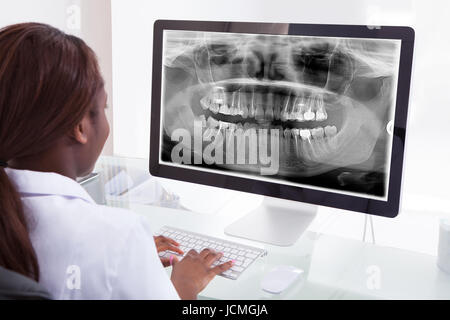 Rear view of female dentist examining jaw Xray on computer in clinic Stock Photo