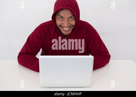 A young internet geek working online. Computer hacker wearing a hooded top using laptop in the dark. The man breaks the access to steal information an Stock Photo