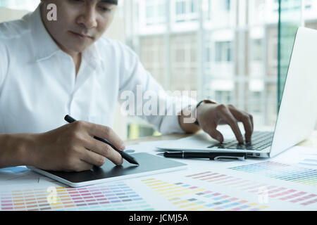 young male graphic designer working with computer and color swatch. creative man using stylus pen and digital tablet at modern office. Architect using Stock Photo