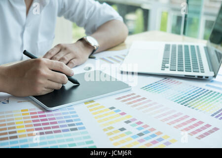 young male graphic designer working with computer and color swatch. creative man using stylus pen and digital tablet at modern office. Architect using Stock Photo