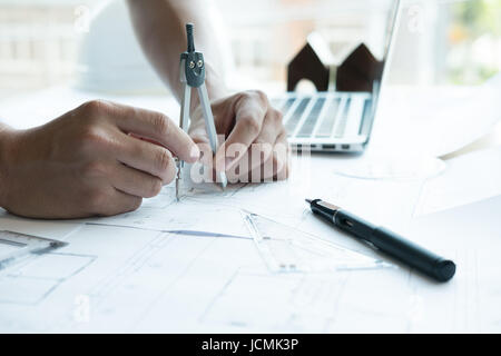 young architect working on real estate project at workplace. Engineer using divider compass at office. Male hand working with living house blueprint.  Stock Photo