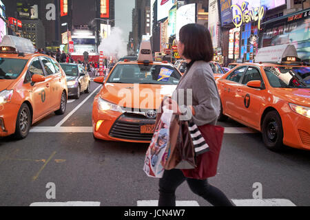 woman crossing crosswalk in front of yellow cabs in the evening in Times Square New York City USA Stock Photo