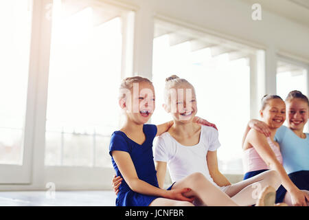 Cute little girls embracing and laughing sitting on floor in ballet class together. Stock Photo