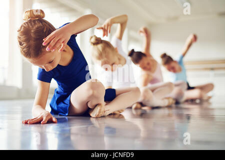 Little ballerinas doing exercises and bending sitting on floor in ballet class. Stock Photo