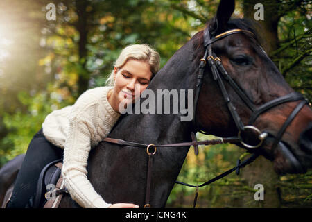Portrait of a blond woman hugging a brown horse while in saddle Stock Photo