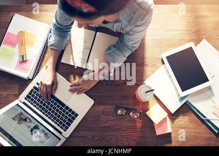 From above young entrepreneur woman sitting and typing a laptop at the workplace in office. Stock Photo