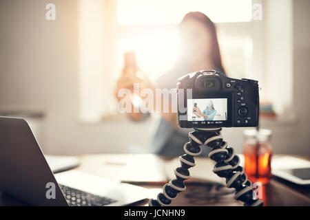 Camera recording young female blogger taking a selfie while making a video podcast. Stock Photo
