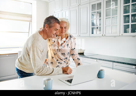 Two elderly people using a laptop computer at the kitchen Stock Photo