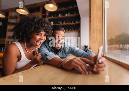 Young couple sitting together at coffee shop and taking selfie using smart phone. Young man and woman laughing while taking selfie in cafe Stock Photo