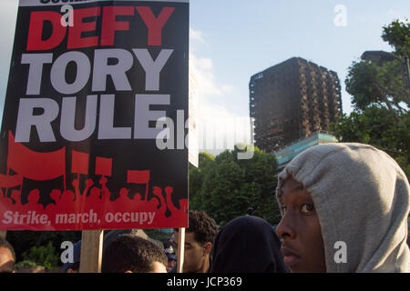 London, UK. 16th June, 2017. A man holds a placard 'Defy Tory Rule' in front of the shell of Grenfell Tower as as people demand justice for those affected by the fire that gutted Grenfell Tower, a residential tower block in west Lodon. Credit: Thabo Jaiyesimi/Alamy Live News Stock Photo