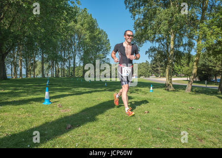Rutland Water, UK. 17th June, 2017. Marcus Dodd, a cheerful, relaxed and tired competitor, trots through a woodland along the shore of Rutland reservoir on a sunny day during the10 km run, the third and final phase of the Dambuster Triathlon (swim, bike and run race) at Rutland Water, England, on 17 June 2017. Credit: Michael Foley/Alamy Live News Stock Photo