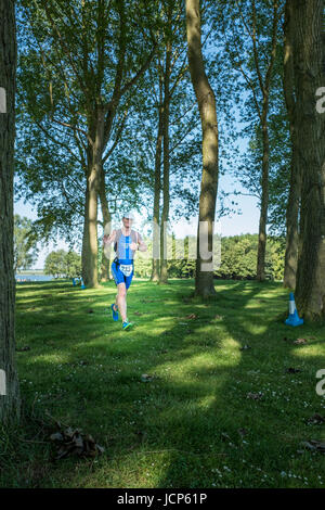 Rutland Water, UK. 17th June, 2017. Iain Darwood, a cheerful, relaxed and tired competitor, gives a wave as he trots through a woodland along the shore of Rutland reservoir on a hot, sunny day during the10 km run, the third and final phase of the Dambuster Triathlon (swim, bike and run race) at Rutland Water, England, on 17 June 2017. Credit: Michael Foley/Alamy Live News Stock Photo