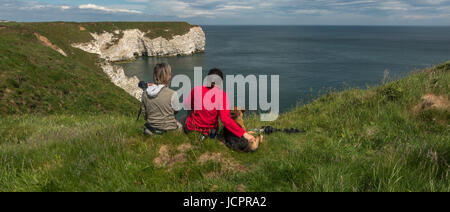 Two women & a dog sitting on clifftops looking out to see watching wildlife, bird spotting with cameras, Flamborough, Yorkshire, England, UK wildlife Stock Photo