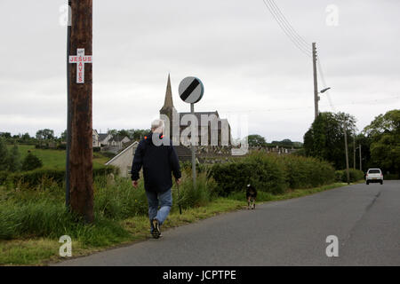 A man walks his dog down the Derryanvil Road close to Drumcree Church, Portadown 20 years since the Drumcree standoff began, Friday June 16th, 2017. The Drumcree conflict or Drumcree standoff is an ongoing dispute over yearly parades in the town of Portadown, Northern Ireland. The Orange Order (a Protestant, unionist organization) insists that it should be allowed to march its traditional route to-and-from Drumcree Church. However, most of this route is through the mainly Catholic/Irish nationalist part of town. The residents, who see the march as sectarian, triumphalist and supremacist, have  Stock Photo