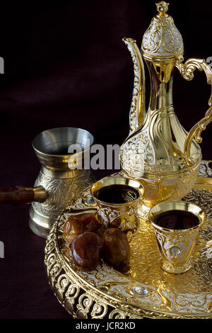 Still life with Traditional golden Arabic coffee set with dallah, coffee pot and dates. Dark background. Vertical photo.