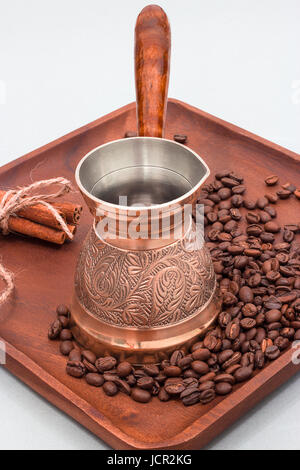 Copper coffee pot with coffee beans and cinnamon sticks. On a wooden plate board. White background Stock Photo
