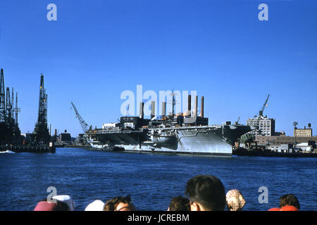 Antique October 1958 photograph, large aircraft carrier at Brooklyn Navy Yard on the East River. The ship is possibly the USS Saratoga (CV/CVA/CVB-60) or the USS Independence (CV/CVA-62). The United States Navy Yard, also known as the Brooklyn Navy Yard and the New York Naval Shipyard, was a shipyard located in Brooklyn, New York. SOURCE: ORIGINAL 35mm TRANSPARENCY. Stock Photo