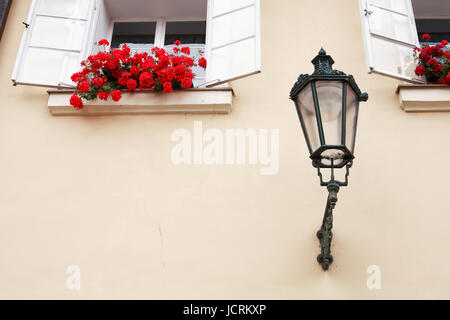 Vintage lantern near open windows with red flowers on the wall of dwelling house Stock Photo