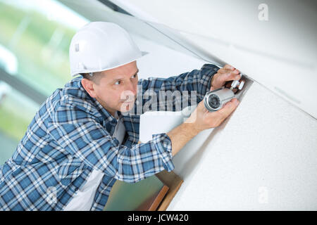 mature male technician fitting cctv camera on wall Stock Photo