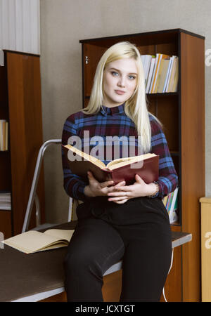young girl student standing and reading book near bookshelves in library background Stock Photo
