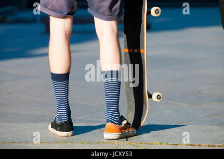 Skateboarding - detail of skateboard and legs with trainers. Stock Photo
