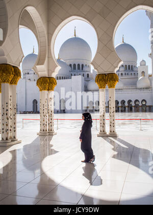 A woman in an abaya and hijab walks beneath arches in the Sheikz Zayed Grand Mosque, Abu Dhabi, United Arab Emirates. Stock Photo