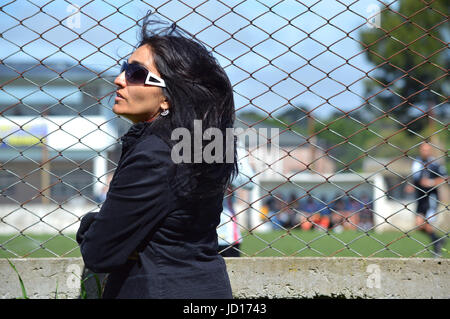 Woman with beautiful black hair looks at the soccer match from the edge of the playing field Stock Photo