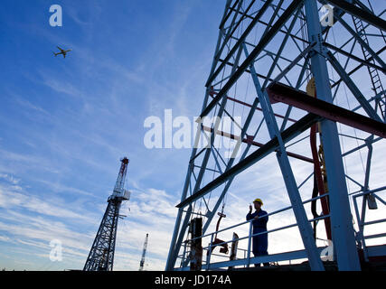 Drilling rig worker talking on radio on platform with airplane flying overhead. Stock Photo