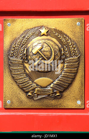 The metal plate at the border post: Golden soviet CCCP - USSR emblem with hammer and sickle on red-green background. Text in different languages. Stock Photo