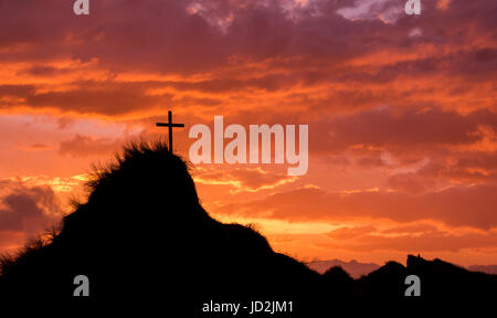 Cross on a tall hill with the sky behind it lit up as the sun goes down. Stock Photo