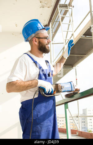 Smiling construction worker in a working outfit and in a protective helmet waving a hand at a hello. Stock Photo