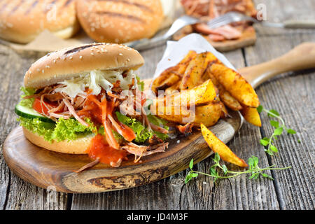 Barbecue pulled pork sandwich with coleslaw, hot BBQ sauce and potato wedges in a paper bag served on a wooden table Stock Photo