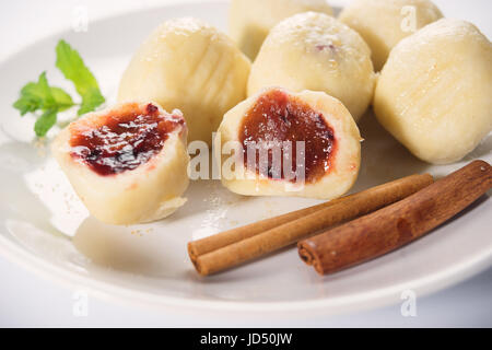 Traditional austrian sween dumplings called Knödels filled with blum and cinnamon were prepared in boiled water and served in a white plate on white b Stock Photo