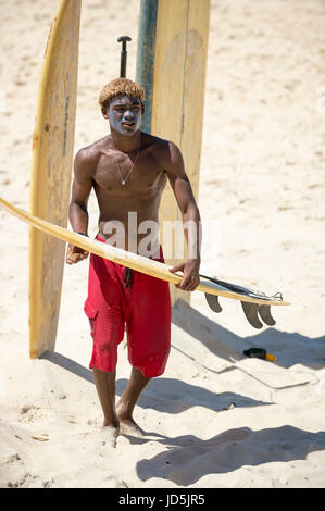 RIO DE JANEIRO - FEBRUARY 10, 2017: Young Brazilian surfer waxes his surfboard along the shore at Arpoador, the popular surf break. Stock Photo