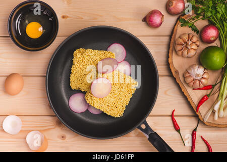 Instant noodles for cooking and eat in the dish with eggs and vegetables on wooden background. Stock Photo