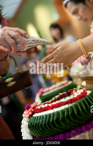 Close-up of holy water being poured on the hands of the bride from elders during a traditional Thai wedding ceremony, Thailand Stock Photo