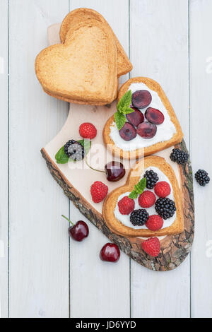 Heart shaped biscuits spread with quark,  cherries and a twig of mint presented on a tree disk