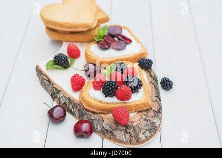 Heart shaped biscuits spread with quark,  cherries and a twig of mint presented on a tree disk