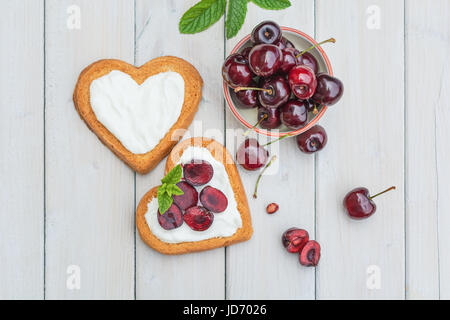 Bowl filled with cherries and heart shaped biscuits spread with quark,  cherries and a twig of mint