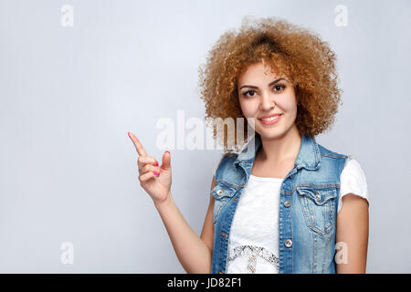 Portrait of beautiful curly mixed race girl in casual style is pointing. looking at camera. studio shot on light gray background. Stock Photo