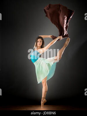 Female ballet dancer on one leg with fabric, studio shot. caucasian fit pretty skinny athletic Stock Photo