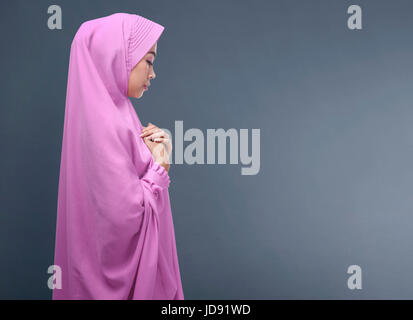 Pretty asian muslim woman with veil praying against dark background Stock Photo