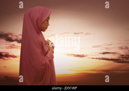 Beautiful asian muslim woman with hijab praying against sunset at sky Stock Photo