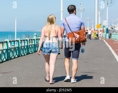 Young couple walking along a seaside promenade holding hands on a very got summers morning in the UK. Stock Photo