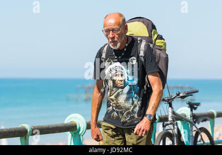 Middle aged man walking along the seafront promenade on a hot morning, carrying a rucksack on his back. Stock Photo