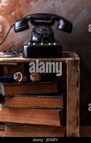 Dusty vintage bakelite phone on a wooden fruit box with old books and sea shells. Stock Photo