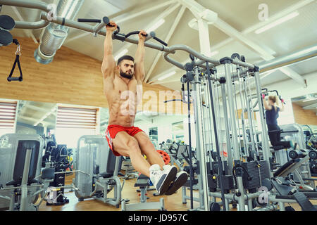 A man doing abs workouts on pull up bar in gym Stock Photo