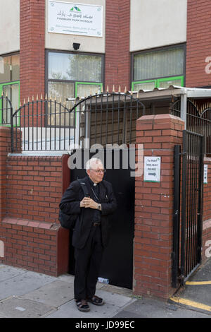 Following the attack on a group of Muslim men outside the Finsbury Park mosque which killed one person and seriously injured another ten, an Anglican minister stands outside the Islamic building where a temporary sign shows where to pray during thew disruption, on 19th June 2017, in the borough of Islington, north London, England. Stock Photo