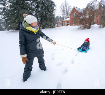 Outdoors at day, mother pulling son on sledge in snow, Ontario, Canada. ontario canada winter cold 2017 snow Stock Photo