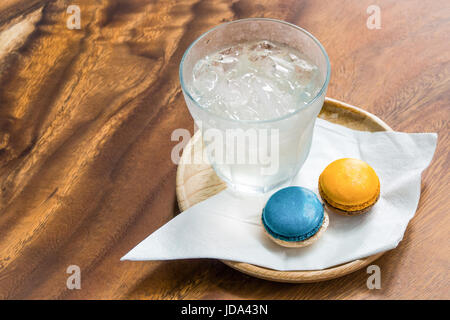 Welcome drink set with fresh ice-water, blue and orange colors magaroons and white nepkin in wooden tray on wooden table. Stock Photo